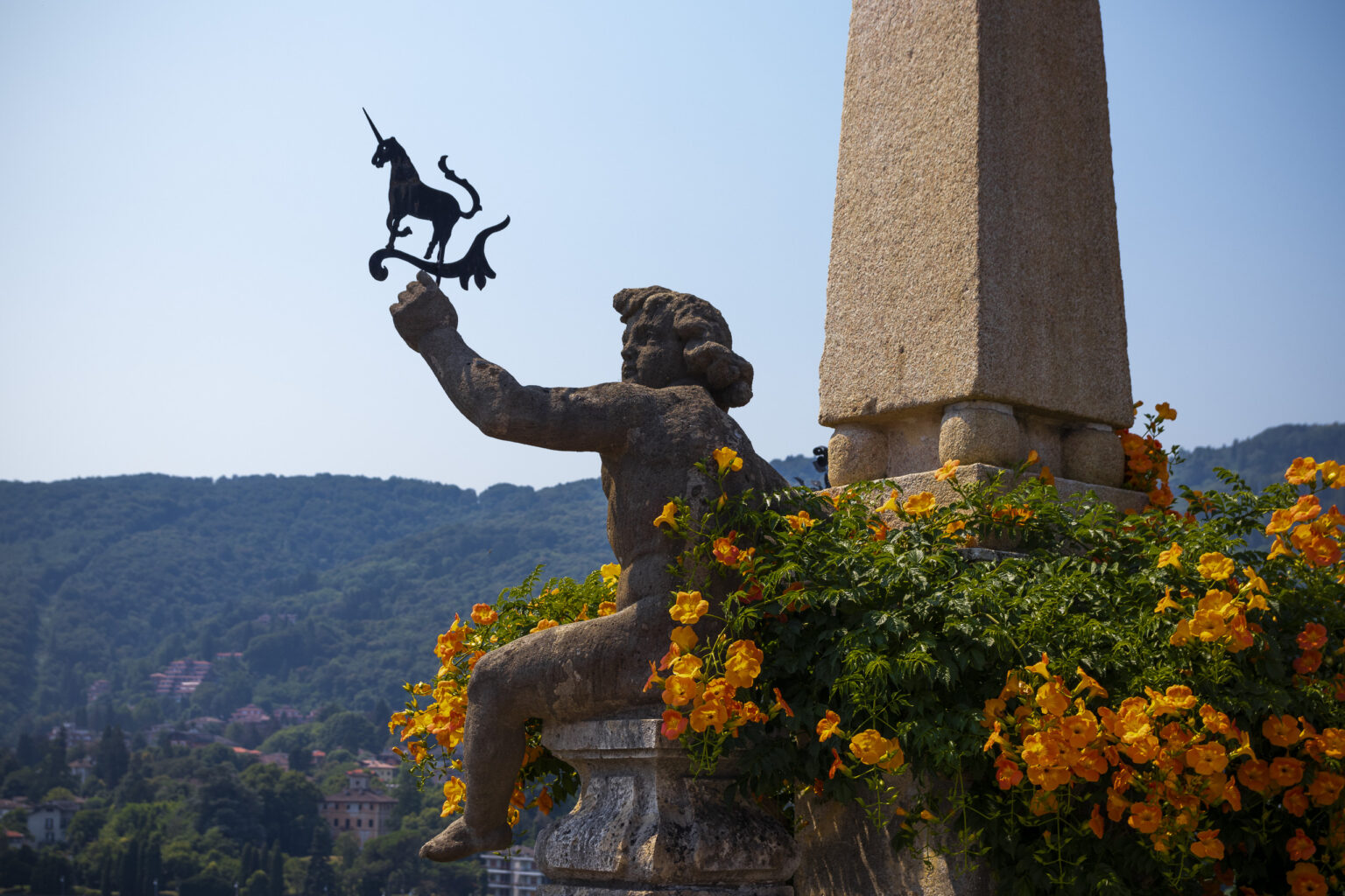 isola bella italie lac majeur lago maggiore jardin sculpture de chérubin tenant une girouette en forme de licorne, symbole de la famille Borromée (Borromeo) entouré de fleurs oranges adossé à un pilier.