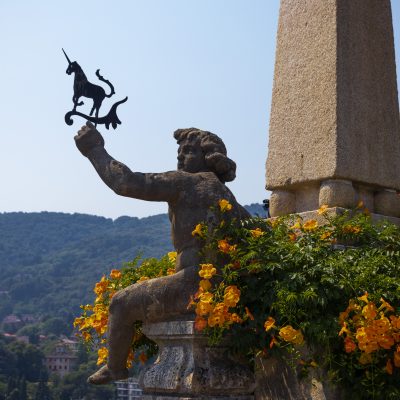 isola bella italie lac majeur lago maggiore jardin sculpture de chérubin tenant une girouette en forme de licorne, symbole de la famille Borromée (Borromeo) entouré de fleurs oranges adossé à un pilier.